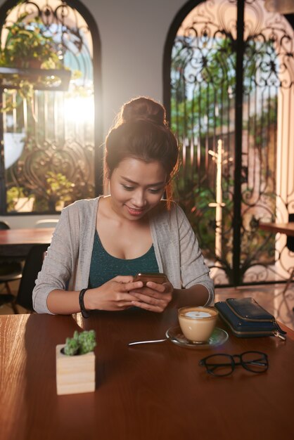 Азиатская молодая женщина текстовых сообщений в кафе