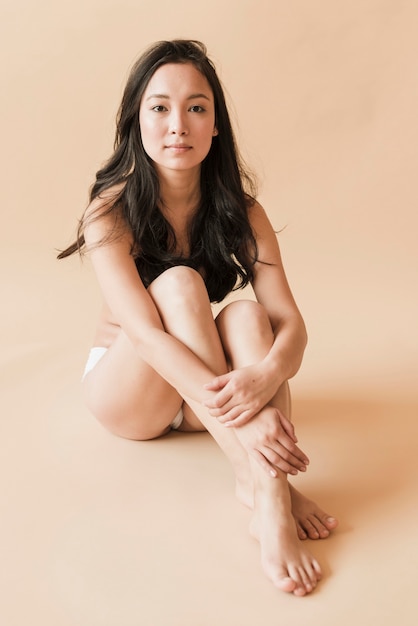 Азиатская молодая женщина в нижнем белье, сидя со скрещенными ногами