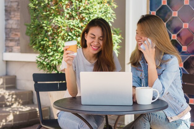 コーヒーを飲んでスマートフォンを使用しているラップトップで働くアジアの若い女性