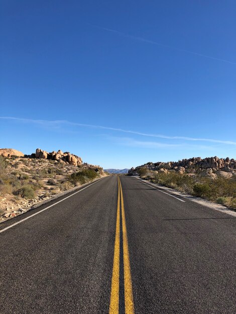 澄んだ青い空の下に黄色い線のあるアスファルト道路