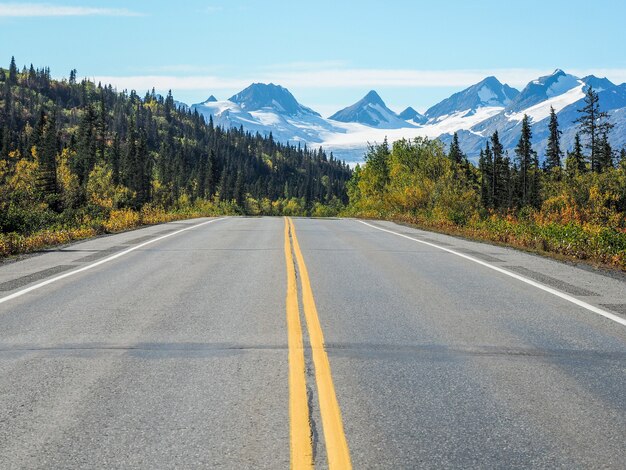Asphalt road with yellow lines and the Worthington Glacier in Alaska