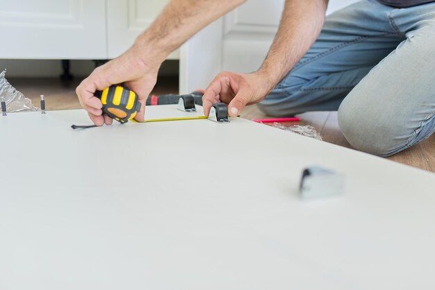 自宅​で​木製​の​白い​家具​を​組み立て​、​大工​の​手​に​道具​と​巻尺​を​付けます​。​改修​、​新しい​家具​、​大工​仕事​の​プロセス
