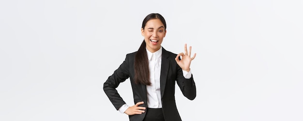 Assertive and confident young asian businesswoman got all under control wink and show okay gesture to encourage deal is done good job nice work or approval gesture standing pleased