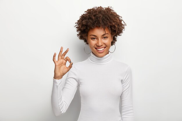 Assertive good looking woman with Afro bushy hairstyle, shows okay gesture