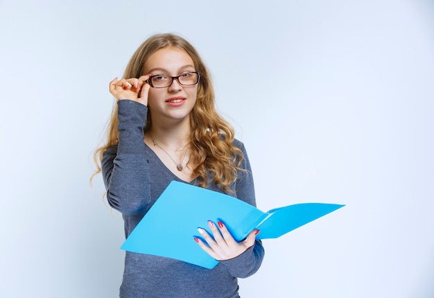 Assistant with eyeglasses holding a blue folder and looks like she has a bright idea or she enjoyed the project