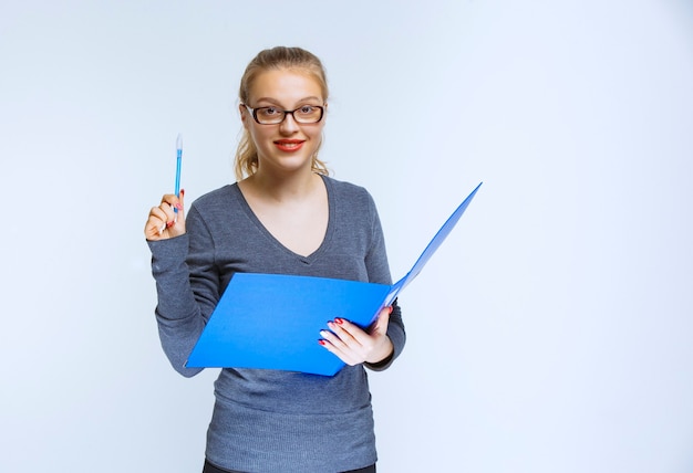 Assistant with eyeglasses holding a blue folder and looks like she has a bright idea or she enjoyed the project.