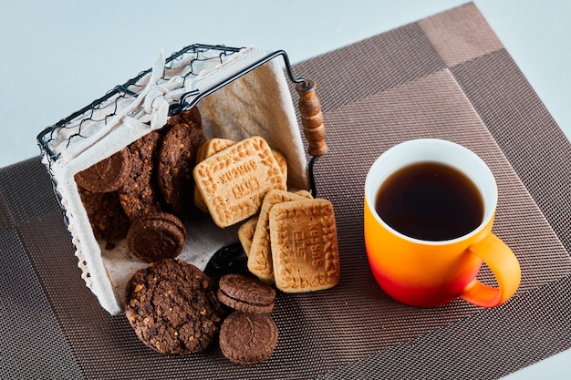 Assorted biscuits, candies and a cup of tea on gray surface.