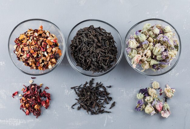 Assorted dried herbs in glass bowls on a plaster surface flat lay.