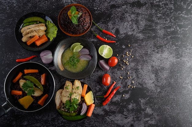 Assorted food and dishes of vegetables, meat and fish on a black stone table. Top view.