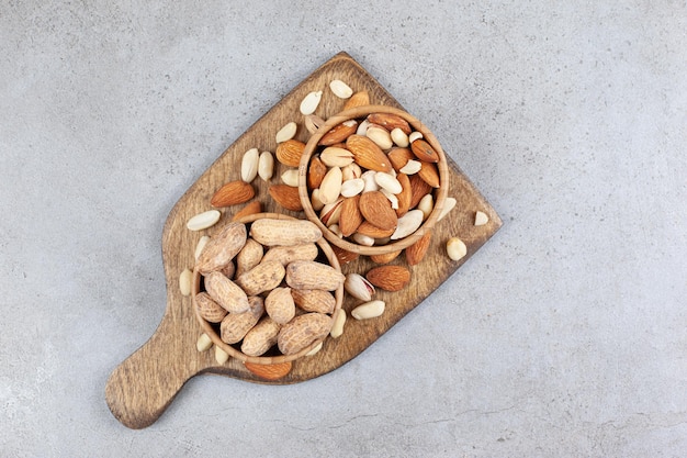 Assorted nuts in wooden bowls and piled on wooden board on marble background. High quality photo