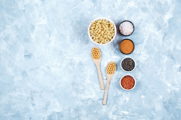 Assorted pasta in bowl and wooden spoons with spices top view on a grungy grey background
