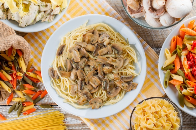 Assorted pasta meals in plates with raw pasta and mushrooms