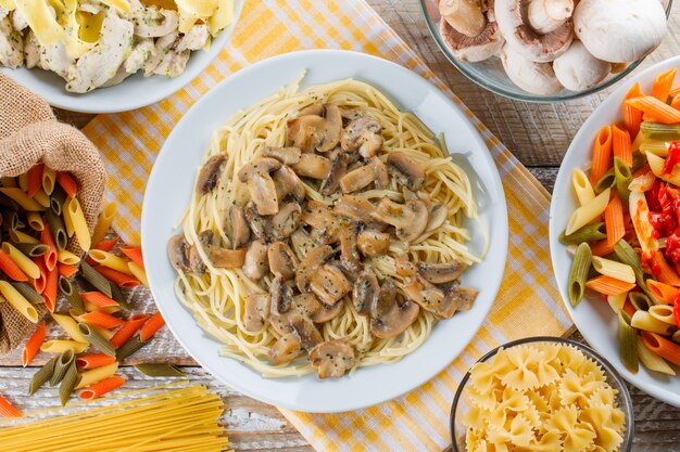 Assorted pasta meals in plates with raw pasta and mushrooms