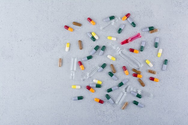 Assorted pharmaceutical capsules and ampoules on marble surface. 