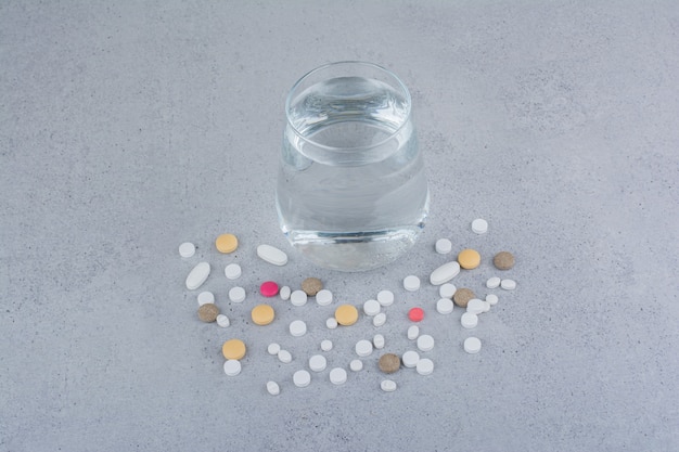 Assorted pharmaceutical medicine pills and glass of water. 