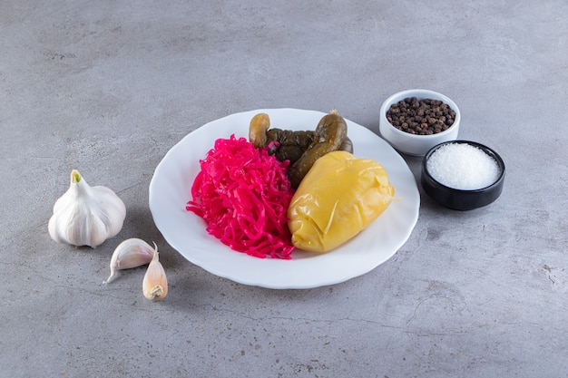 Assorted pickles vegetables placed on a stone surface.