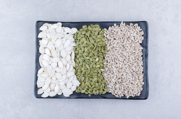 Assorted plate of pepitas, sunflower seeds and white pumpkin seeds on marble surface