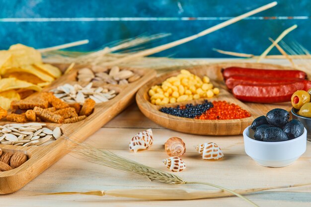 Assorted snacks, a plate of sausages, caviar, and olives on a wooden table.