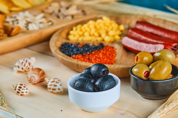Assorted snacks, a plate of sausages, caviar, and olives on a wooden table.