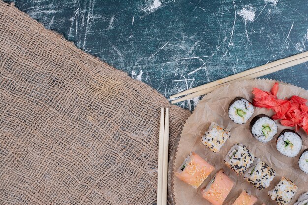 Assorted sushi rolls served on wooden platter with pickled ginger and chopsticks.