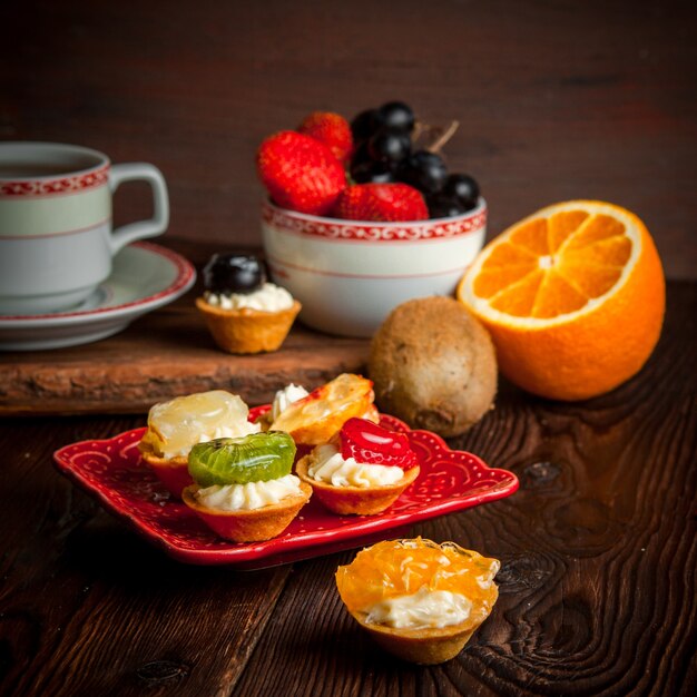 assorted tartlets with cup of tea and fruit platter and orange in plate