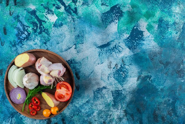 Assorted vegetables and chicken drumstick on a wooden plate, on the blue background. 