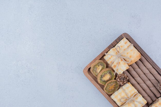 Assortment of biscuits and dried kiwi on wooden board. 