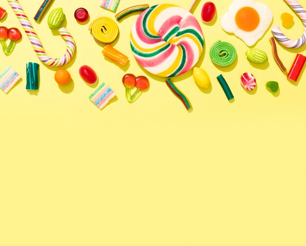 Assortment of colorful candies on yellow background with copy space