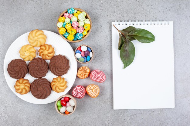 Assortment of cookies, candies and marmelade next white board and leaves on marble background. High quality photo