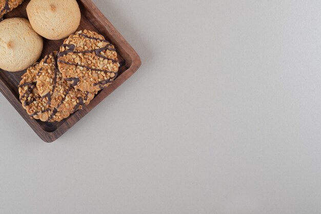 Assortment of cookies on a small wooden tray on marble background.