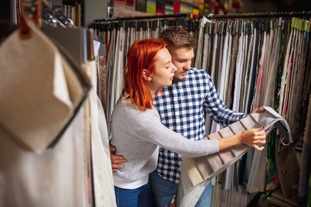 Assortment. Couple choosing textile at home decoration store, shop. Making of home interior design during quarantine. Happy man and woman, young family look dreamful, cheerful choosing materials.