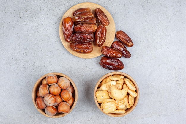 An assortment of dates on wooden board and nuts and biscuits in bowls on marble background. High quality photo