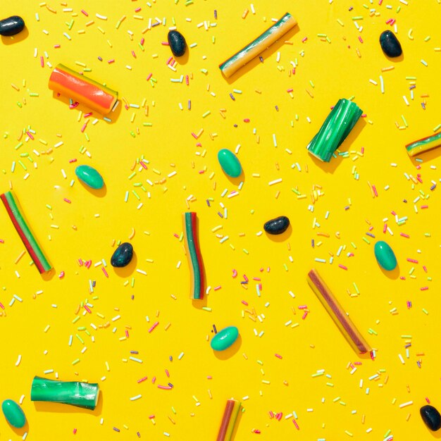 Assortment of different colored candies on yellow background