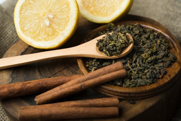 Assortment of dry tea herbs with halved lemons on wooden tray