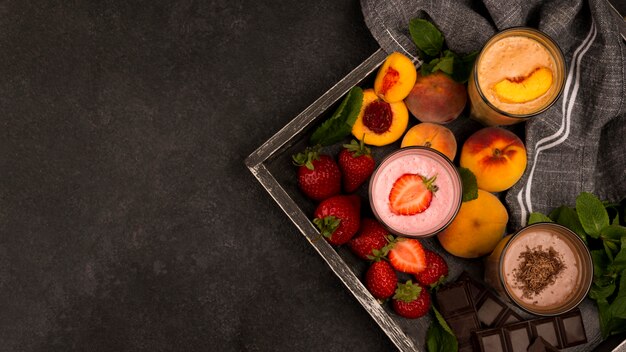 Assortment of milkshake glasses on tray with fruits and chocolate