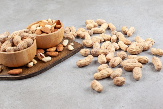 Assortment of nuts in bowls on wooden board and scattered on marble background. High quality photo