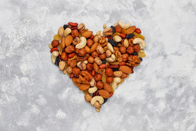 assortment of nuts shape of heart cashew, hazelnuts, walnuts, pistachio, pecans, pine nuts, peanut, raisins.top view