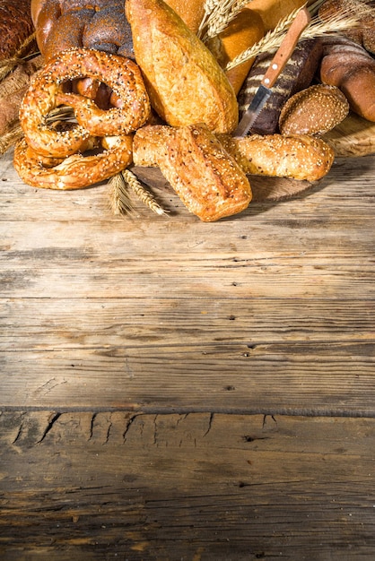 木製の素朴な背景のコピースペースに、さまざまなおいしい焼きたてのパンの品揃え Premium写真
