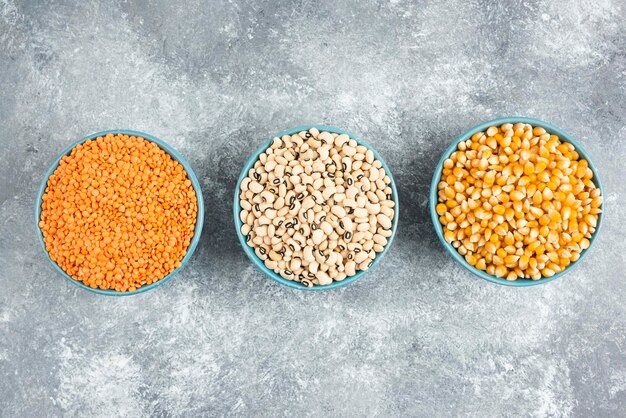 Assortment of raw beans, corn kernels and red lentils on marble table.