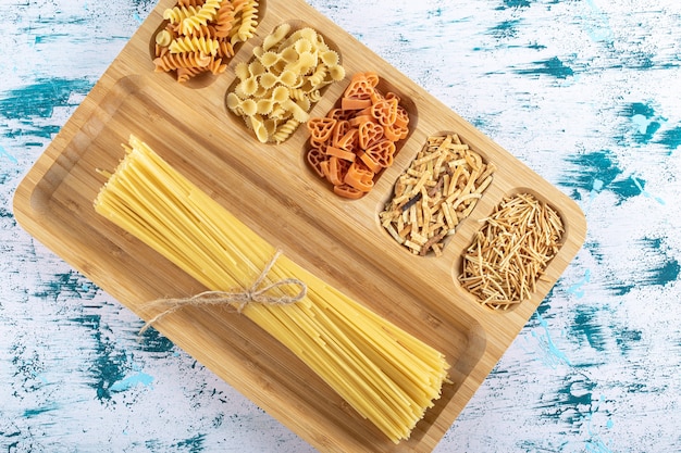 Foto gratuita assortimento di pasta cruda posta sul piatto di legno.