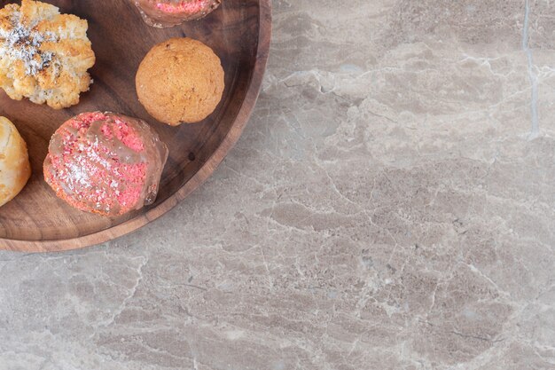 Assortment of various cookies on a wooden tray on marble surface