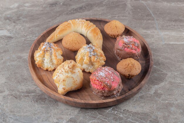 Assortment of various cookies on a wooden tray on marble surface