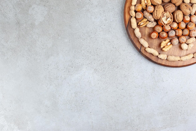 An assortment of various nut types on wooden board on marble background.