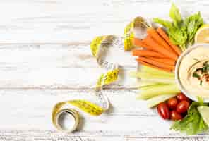 Free photo assortment of vegetables on plate with hummus and measuring tape