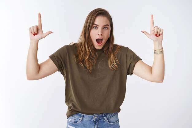 Astonished amazed speechless gorgeous young tomboy woman wearing olive t-shrir raising index finger pointing up incredible offer promo drop jaw impressed surprised, widen eyes white background