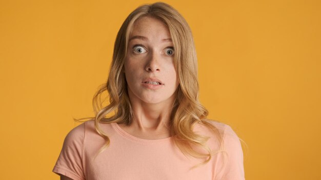 Astonished blond girl scaredly  looking in camera over colorful background Afraid expression