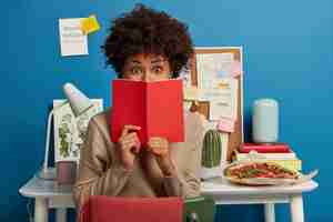 Free photo astonished college student covers face with red diary, shocked to forget about important task to prepare