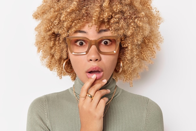 無料写真 驚いた巻き毛の女性は、予期しないニュースに驚かされて、あごを見つめ続けます白い背景の上に隔離された大きな眼鏡とカジュアルなタートルネック人間の反応の概念