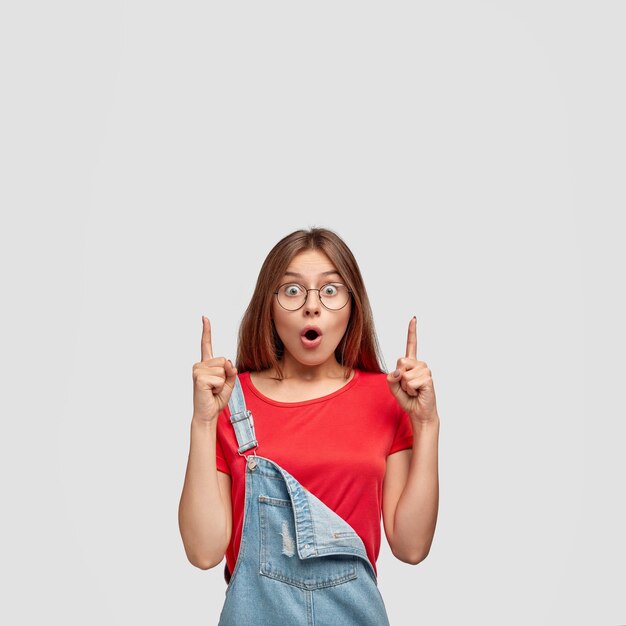 Astonished cute European teenage girl with dark straight hair, healthy skin, dressed in casual clothes