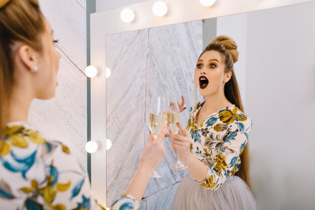 Astonished happy young woman with stylish coiffure in mirror in hairdresser salon